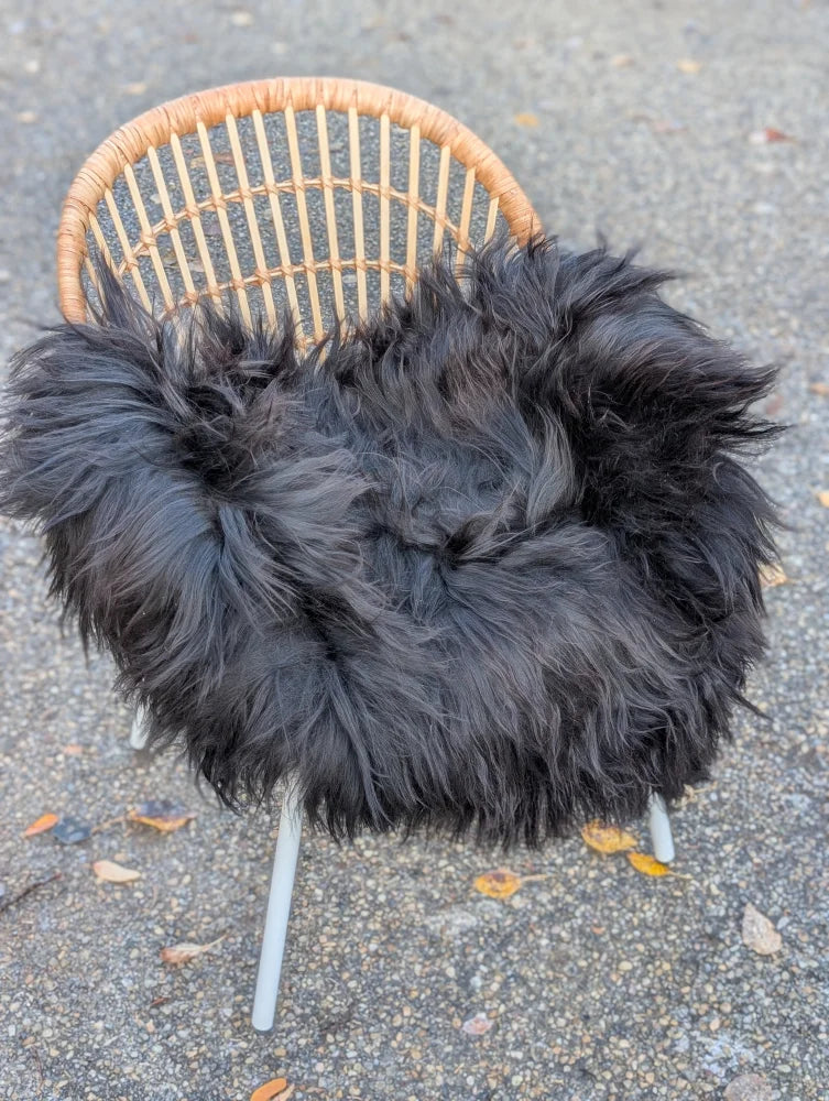 Black fluffy wool icelandic sheepskin long wool throw draped over a wicker chair for cozy decor