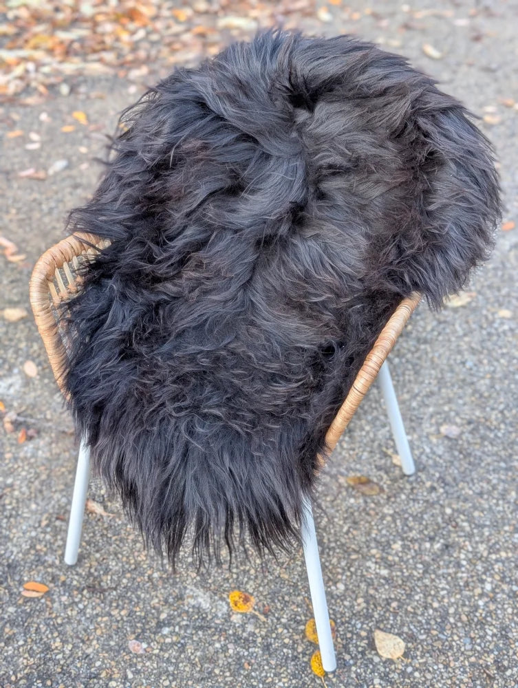 A plush thick black long wool icelandic sheepskin rug draped over a wicker chair with white metal legs
