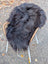 A plush thick black long wool icelandic sheepskin rug draped over a wicker chair with white metal legs