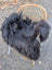 Black long wool icelandic sheepskin throw draped over wicker chair showcasing natural wool icelandic texture