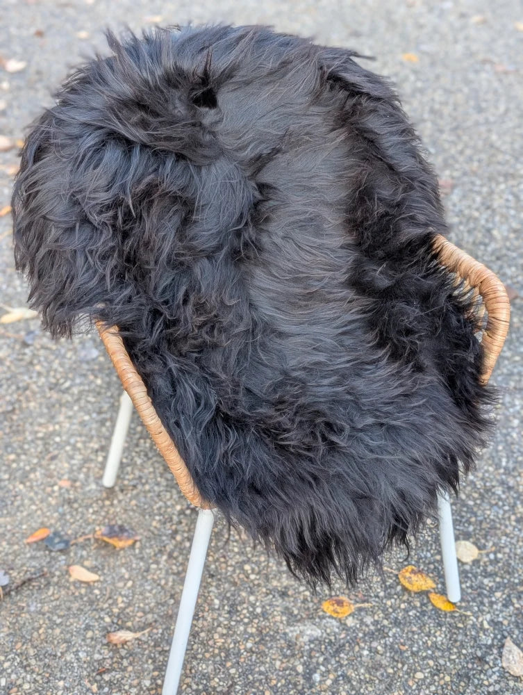 A plush black long wool icelandic sheepskin throw draped over a chair with wicker arms and white metal legs