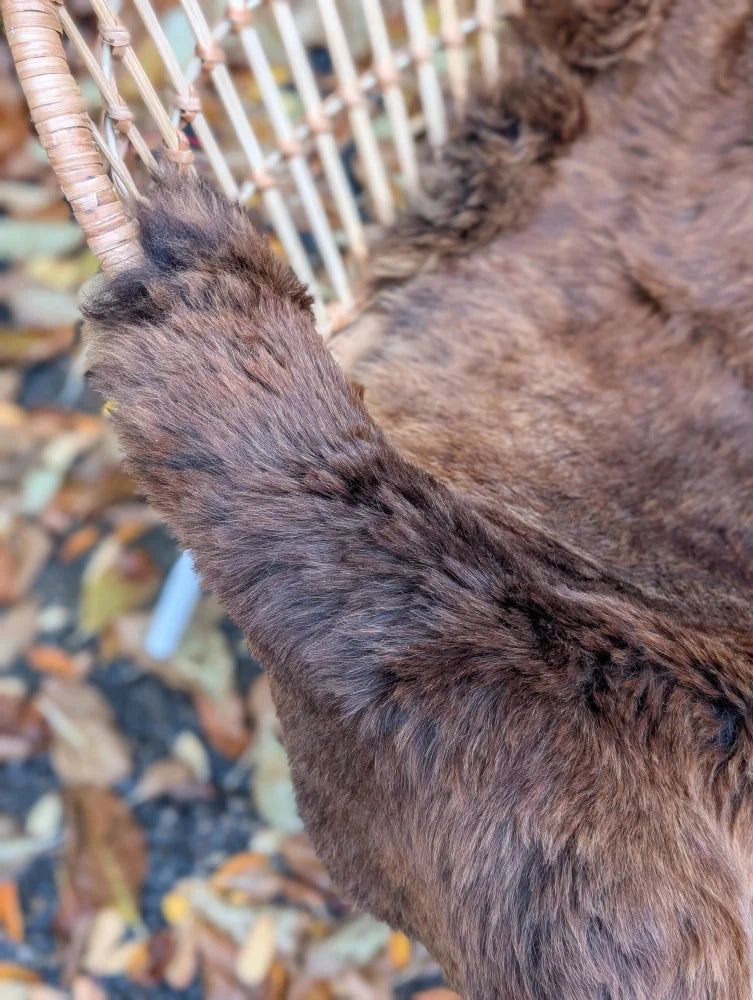A plush brown wool icelandic sheepskin blanket draped over a woven wicker chair for cozy comfort