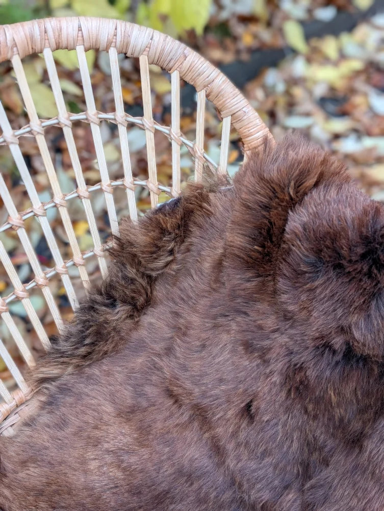 A plush rich brown icelandic sheepskin rug with soft fluffy wool resting on a woven wicker chair