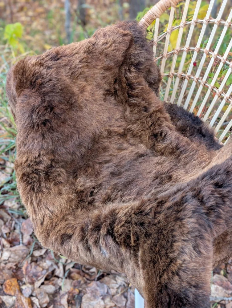A plush brown wool icelandic sheepskin short fur throw draped over a wicker chair for cozy decor