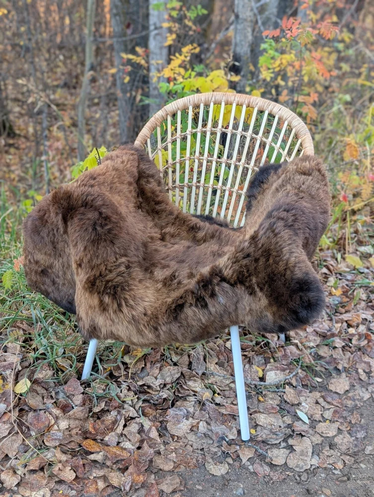 A cozy thick brown wool icelandic sheepskin throw draped over a woven rattan chair with white metal legs