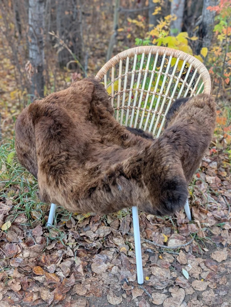 Brown faux fur throw draped over wicker chair with white metal legs made from wool icelandic sheepskin material