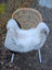 A cozy white long wool icelandic sheepskin rug draped over a wicker chair with slender white legs and dark edges
