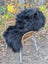 Black thickly fur-covered wool icelandic sheepskin throw blanket draped over wicker chair long wool natural black