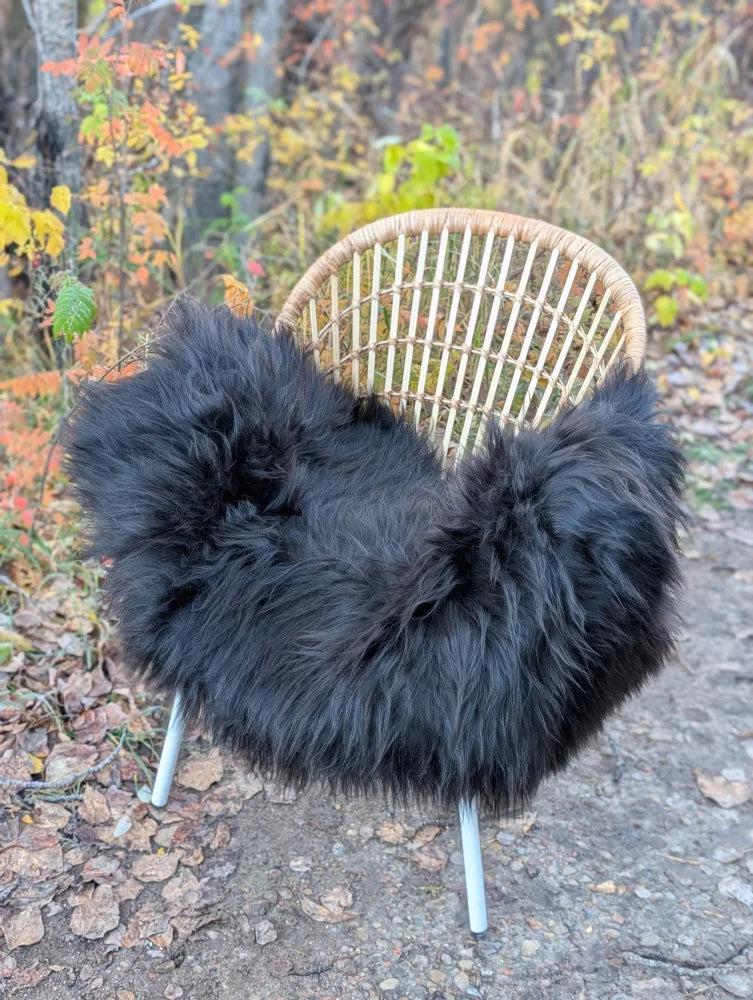 A cozy black wool icelandic long wool sheepskin throw draped over a wicker chair with metal legs