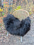 A cozy black wool icelandic long wool sheepskin throw draped over a wicker chair with metal legs