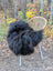 Black fluffy icelandic sheepskin long wool throw draped over wicker chair with metal legs for cozy use