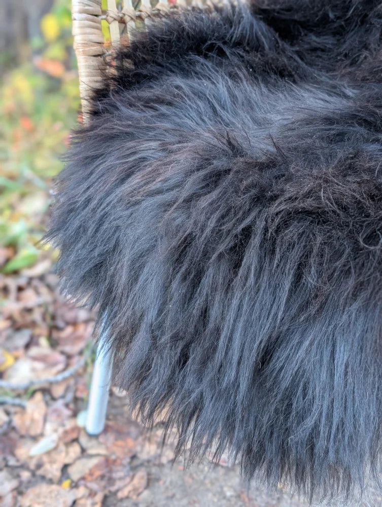 A plush icelandic sheepskin throw in natural black with long wool draped over a woven chair for cozy use