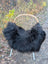 Black fluffy icelandic sheepskin throw with long wool draped over a wicker chair with metal legs for cozy decor