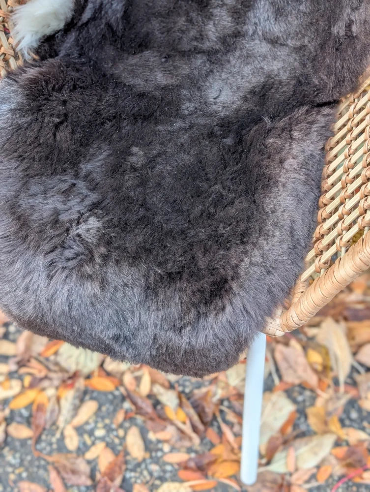 A plush dark gray wool icelandic sheepskin throw with dark edges draped over a wicker chair