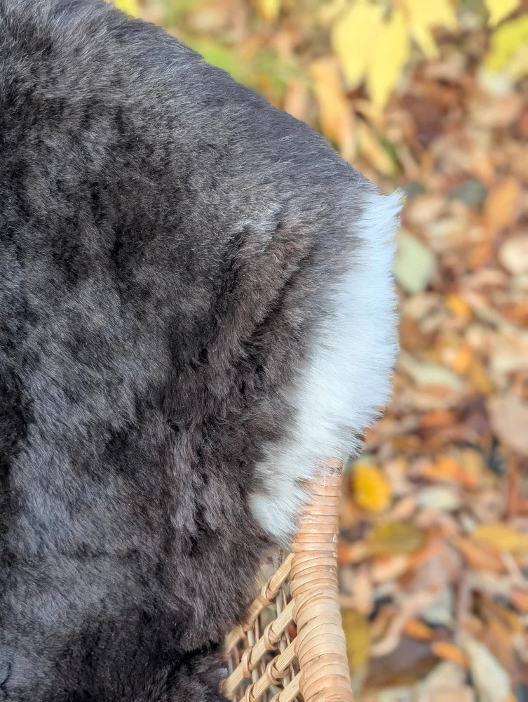 A fluffy dark gray and white rabbit tail on a woven wicker surface next to a wool icelandic sheepskin rug with dark edges