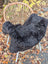 Black plush wool icelandic sheepskin rug with dark edges draped over a wicker chair perfect for cozy decor