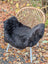 A cozy black wool icelandic sheepskin chair cover with dark edges draped over a wicker chair with white metal legs