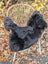 Black short wool icelandic sheepskin chair cover with dark edges draped over a wicker chair for cozy seating