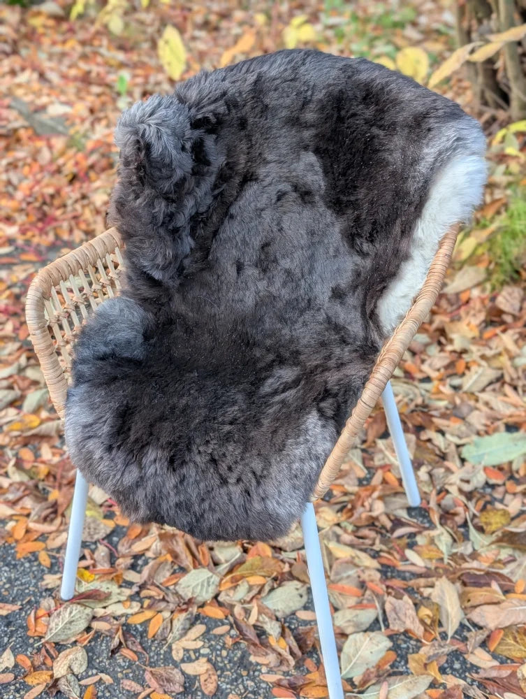 A dark gray wool icelandic sheepskin rug with soft fluffy texture and subtle white accents draped over a wicker chair