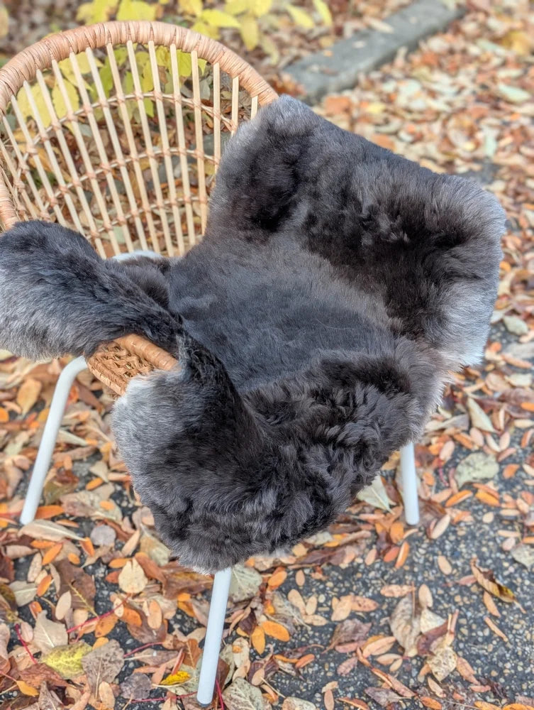 Dark gray plush ice68 wool icelandic sheepskin cover with dark edges draped over a wicker chair
