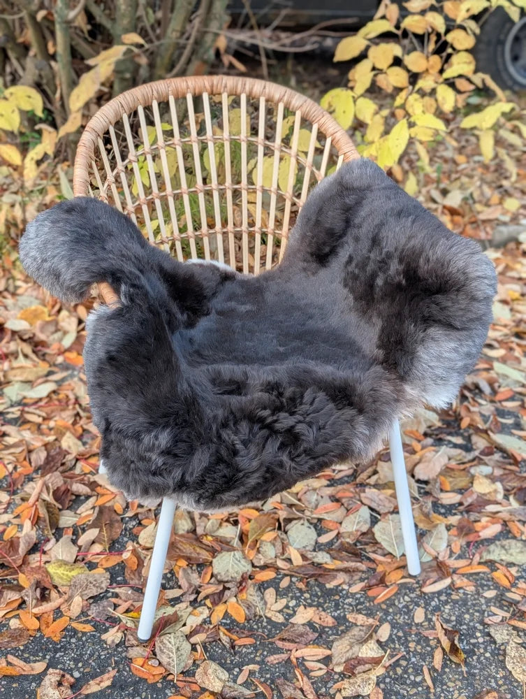 A plush dark gray wool icelandic sheepskin cover with dark edges draped over a woven wicker outdoor chair