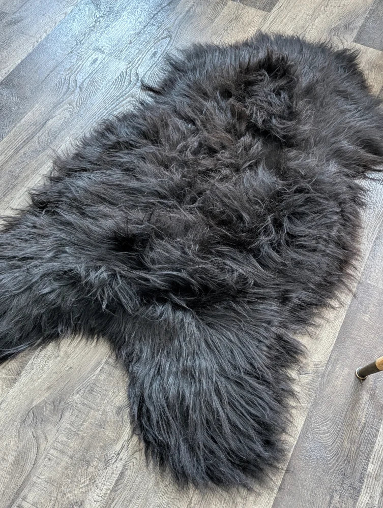 A plush dark gray natural blacky long wool icelandic sheepskin rug lying on a wooden floor
