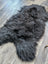 A plush dark gray natural blacky long wool icelandic sheepskin rug lying on a wooden floor
