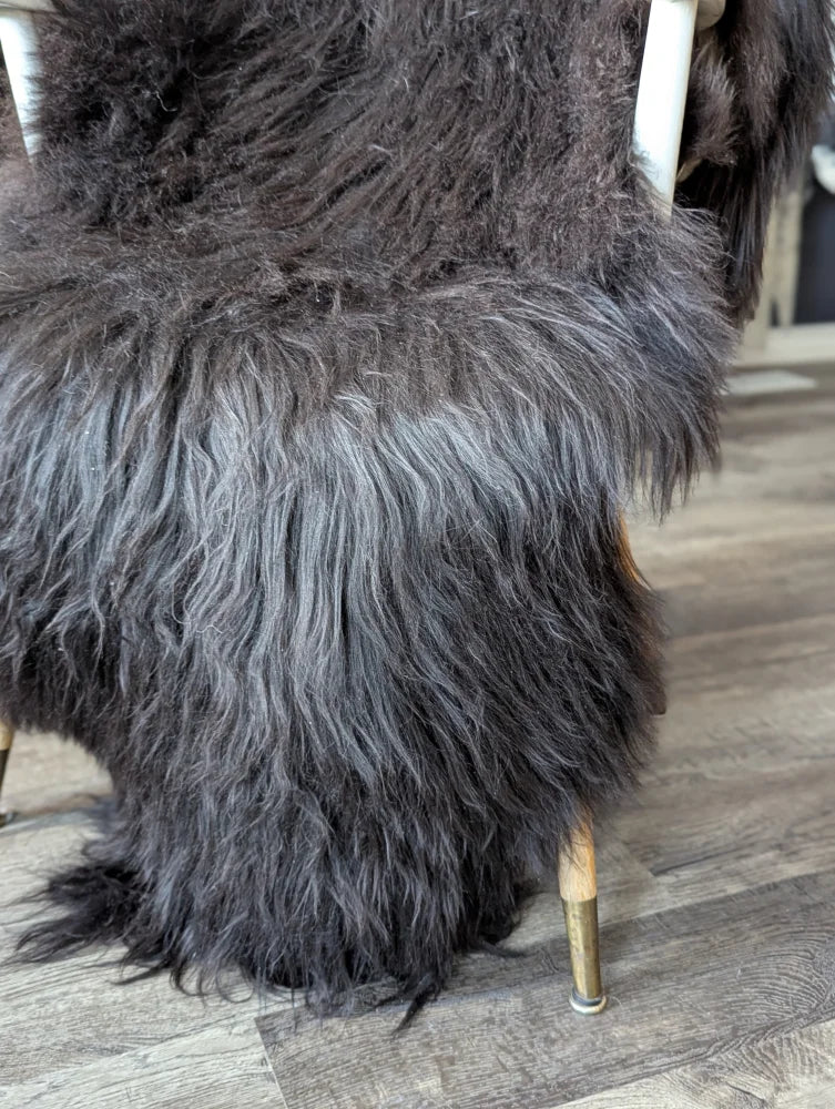 A plush dark gray icelandic sheepskin with long wool natural blacky fur draped over the back of a chair