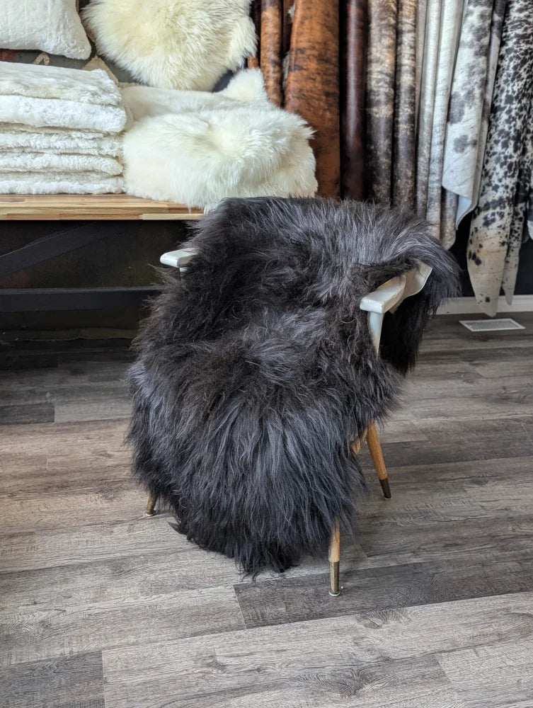 Dark gray thickly textured natural blacky long wool icelandic sheepskin draped over a modern chair with light wood legs