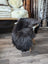 Dark gray thickly textured natural blacky long wool icelandic sheepskin draped over a modern chair with light wood legs
