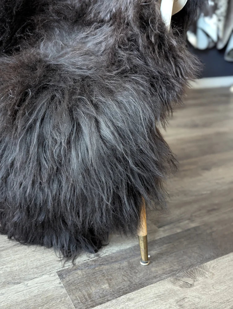 A plush dark gray faux fur chair with wooden legs and brass base featuring natural blacky long wool icelandic sheepskins