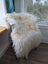 A plush off-white long wool icelandic sheepskin throw draped over a white wooden chair with black metal legs