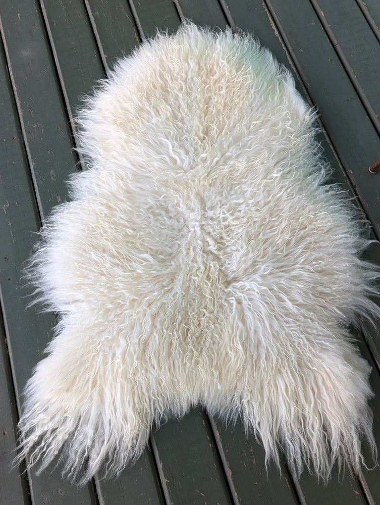 A plush off-white icelandic sheepskin rug with long curly wool and a natural irregular shape perfect for cozy decor