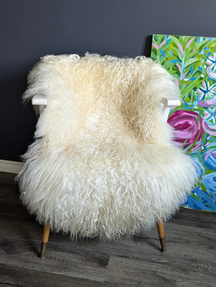 Cream-colored curly sheepskin chair with white wooden arms and legs featuring long wool icelandic sheepskins