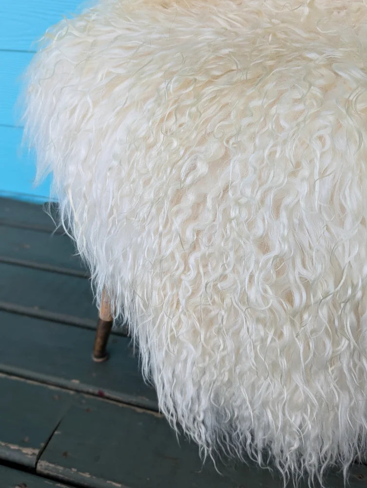 A plush off-white stool covered with natural long wool icelandic curly sheepskin and wooden legs
