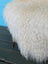 A plush off-white stool covered with natural long wool icelandic curly sheepskin and wooden legs