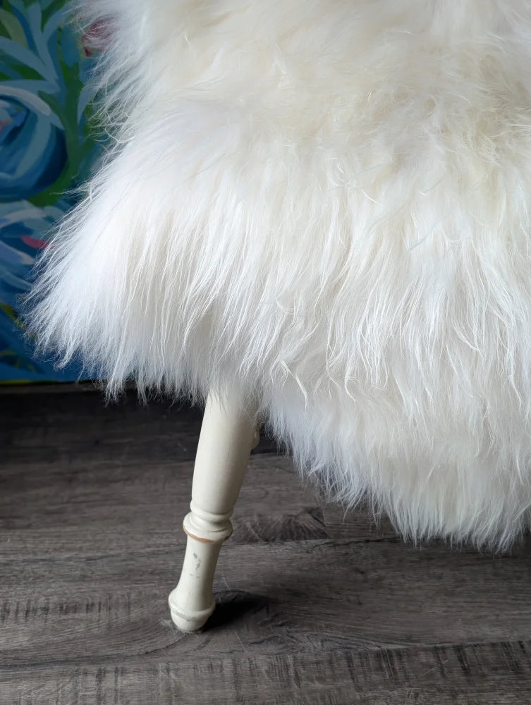 A plush natural white icelandic sheepskins ottoman with long wool and vintage cream wooden legs