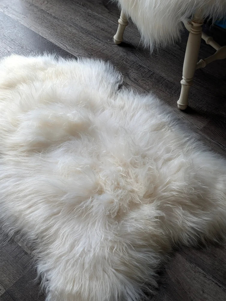 A plush natural white icelandic sheepskin rug with long wool lying on a dark wooden floor