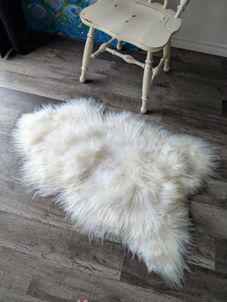 A plush natural white icelandic sheepskin rug with long wool fibers on a dark wood floor perfect for cozy spaces