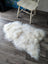 A plush natural white icelandic sheepskin rug with long wool fibers on a dark wood floor perfect for cozy spaces