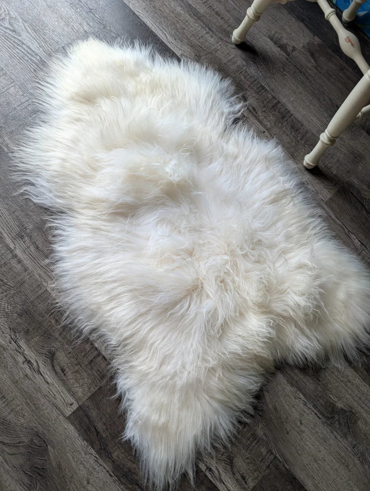 A plush natural white icelandic sheepskin rug with long wool lying on a dark wood floor