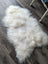 A plush natural white icelandic sheepskin rug with long wool lying on a dark wood floor