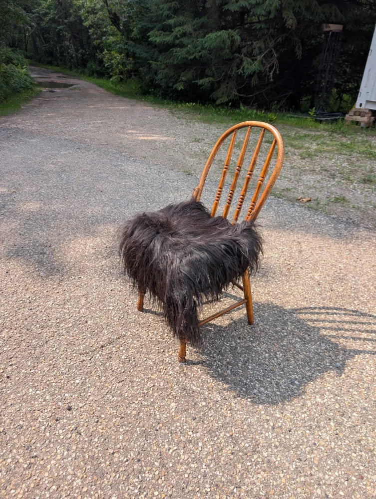 A rustic wooden chair with curved back draped in natural black icelandic sheepskin faux fur throw