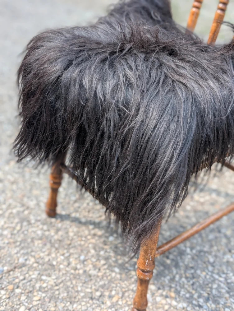 A plush natural black icelandic sheepskin chair square with long shaggy strands draped over a wooden chair
