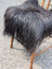 A plush natural black icelandic sheepskin chair square with long shaggy strands draped over a wooden chair
