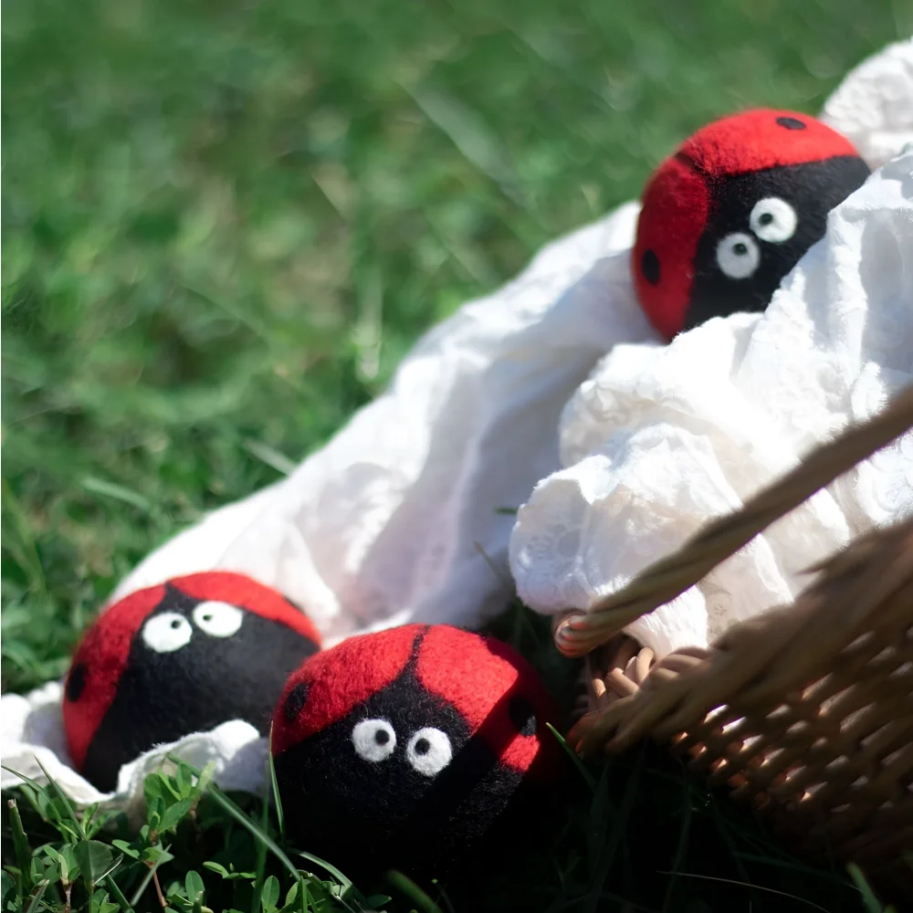 Three plush ladybug trio eco dryer balls in red and black wool nestled in white fabric next to a woven basket