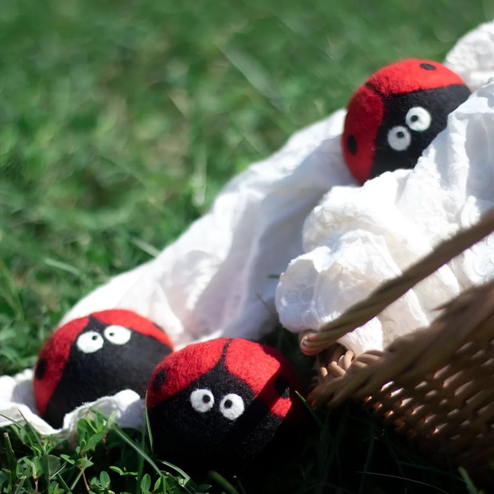 Three plush ladybug trio eco dryer balls in red and black wool nestled in white fabric next to a woven basket