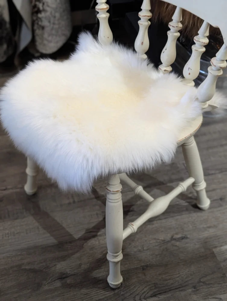 White fluffy merino sheepskin chair pad resting on a distressed white wooden chair for cozy seating