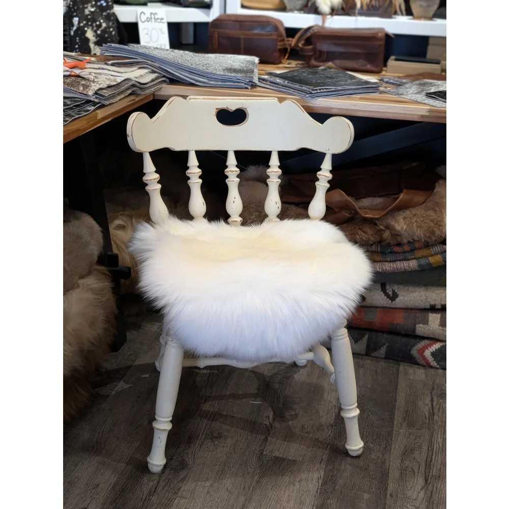A white wooden chair with a heart cutout featuring a fluffy off-white merino sheepskin chair pad seat cushion