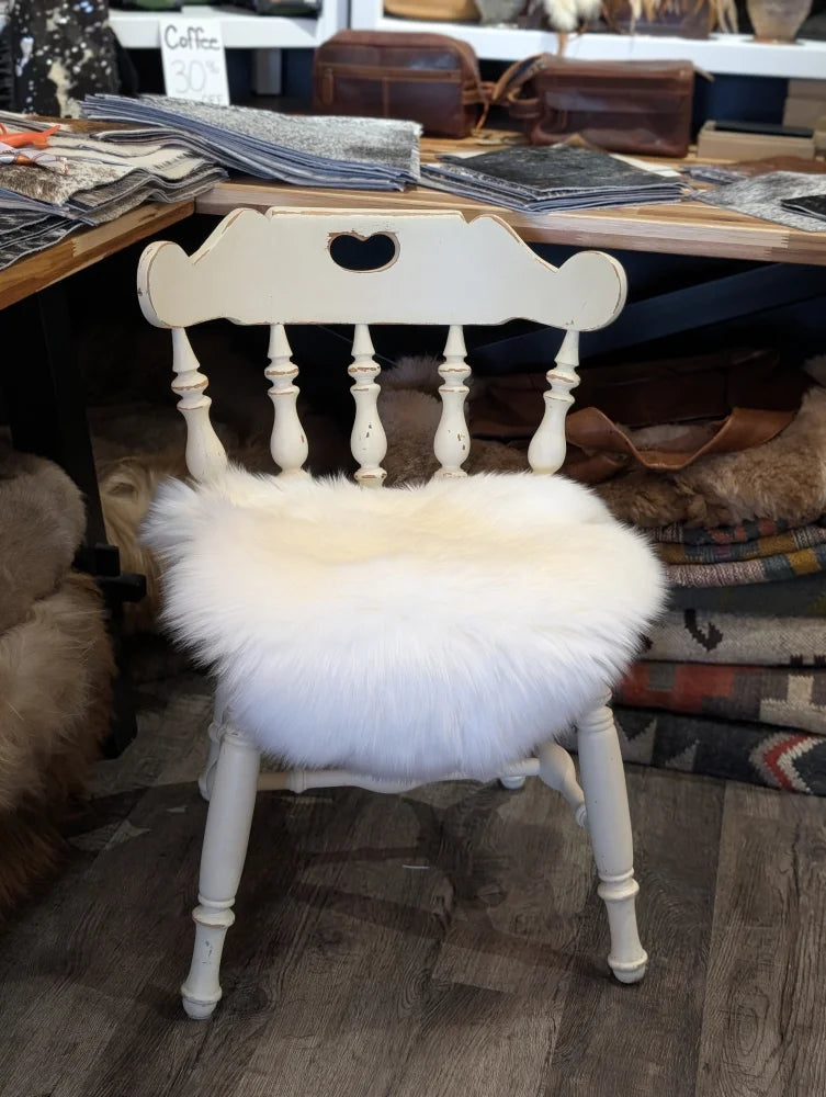 A white wooden chair with a heart cutout featuring a fluffy off-white merino sheepskin chair pad seat cushion
